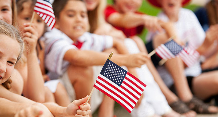 Close-up photo of a group of children sitting down holding miniature american flags