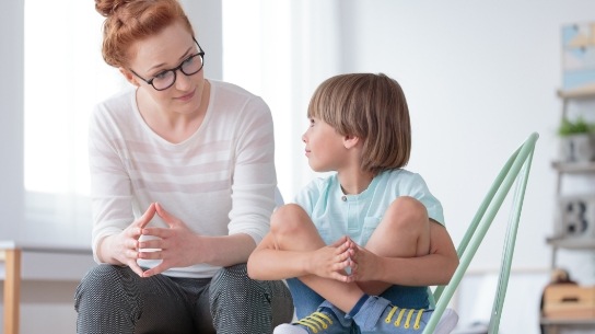 therapist taking with child with legs crossed on chair